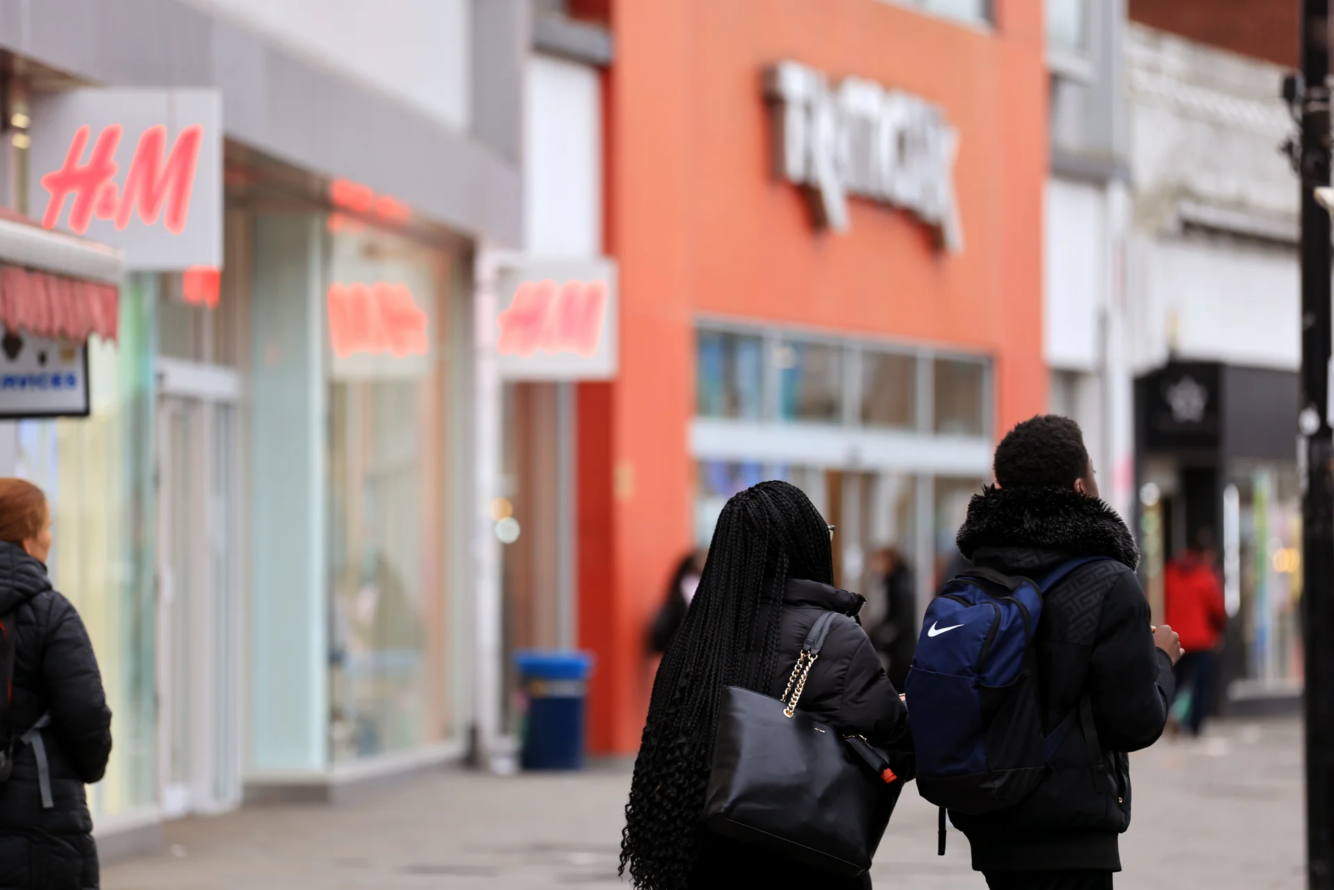 Exterior view of TK Maxx and H&M stores at Lewisham Shopping Centre. Shoppers walk past on a cloudy day.