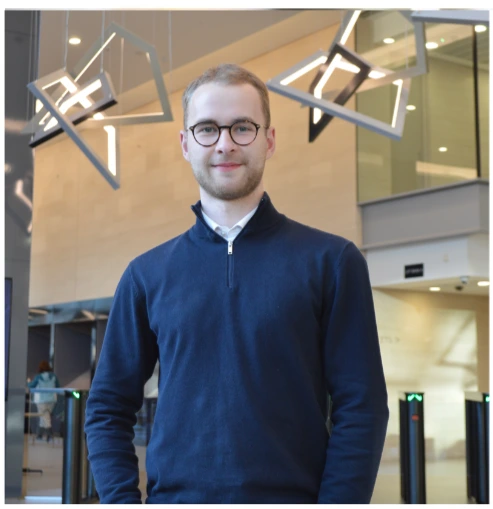 Person in glasses and blue sweater indoors with modern lighting.