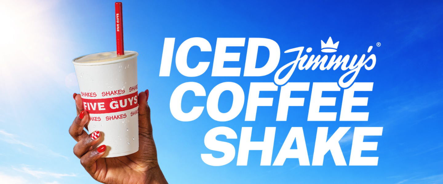 Hand holding a Five Guys cup with a Jimmy’s iced coffee shake against a bright blue background.