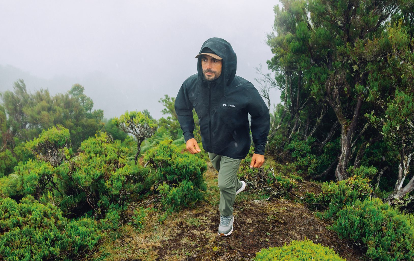 A man in a rain jacket hiking up a mountain 