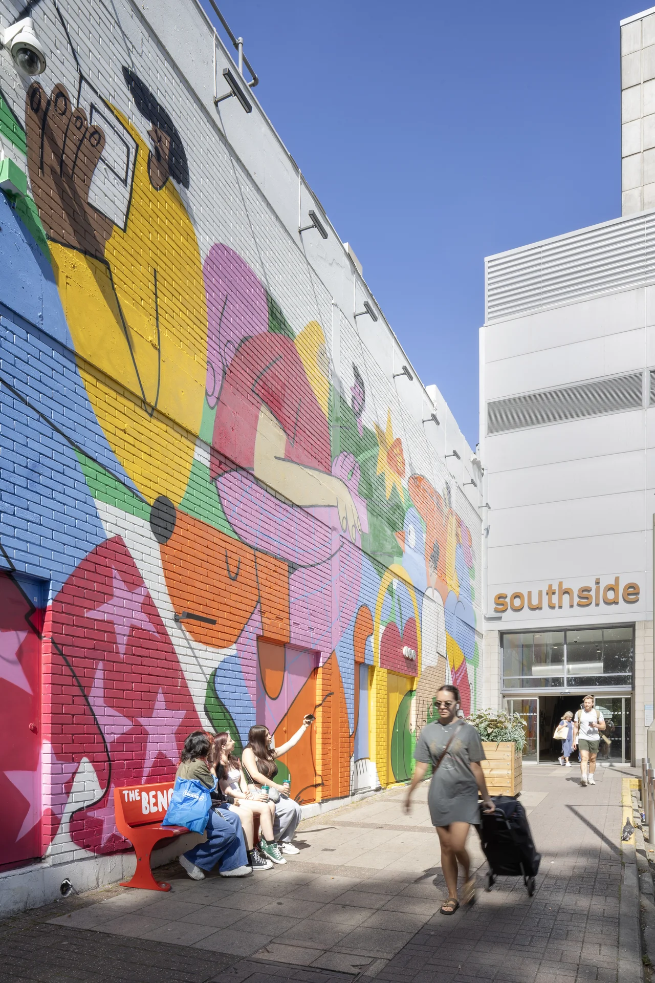 The brightly colored, abstract **mural art** facade at the entrance to **Southside Shopping Centre** in Wandsworth, with shoppers sitting on a bench and others passing by.