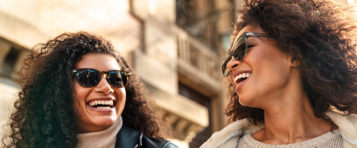 Two women in sunglasses smiling at one another