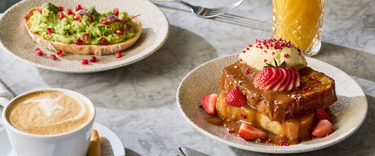Avocado toast, strawberry French toast, a coffee, and a juice on a marble table