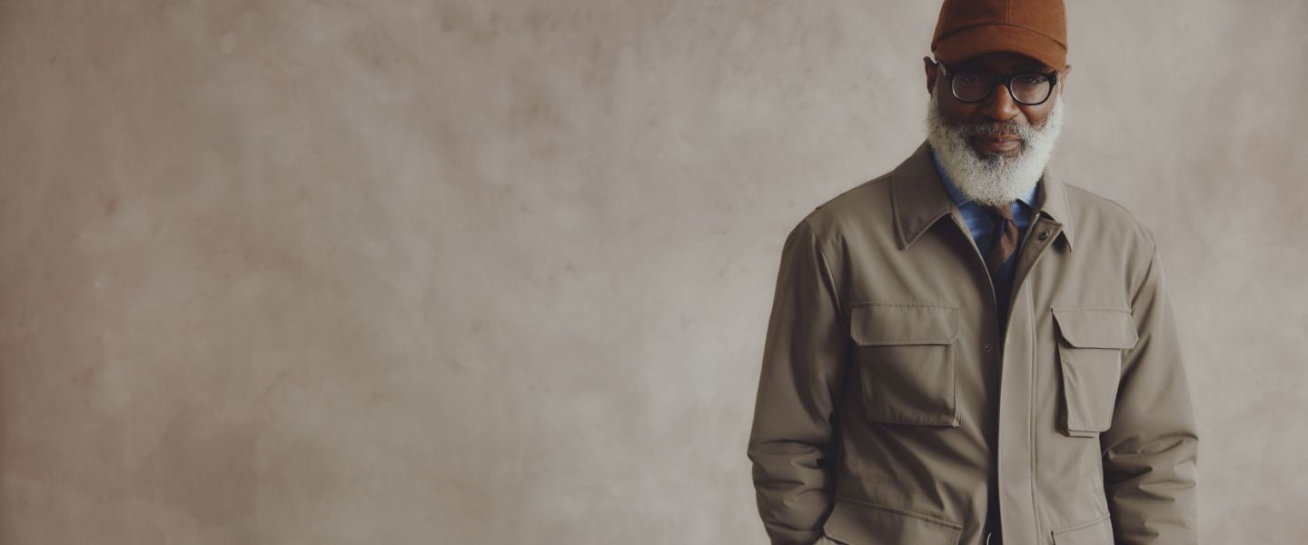 A man wearing a taupe jacket in front of a beige background