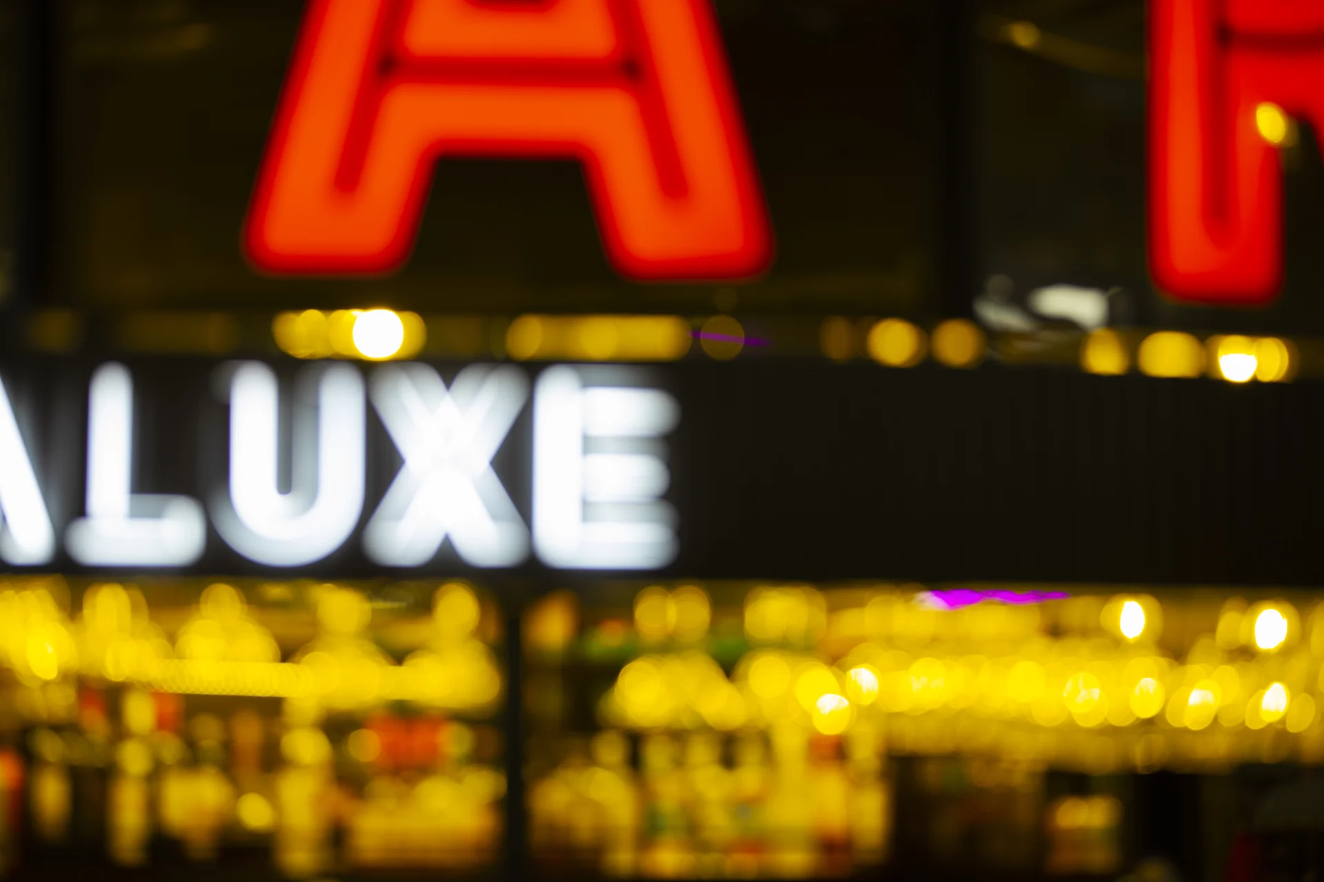 Blurred nighttime scene with bright red and white neon signs, warm yellow lights, and a bar interior.