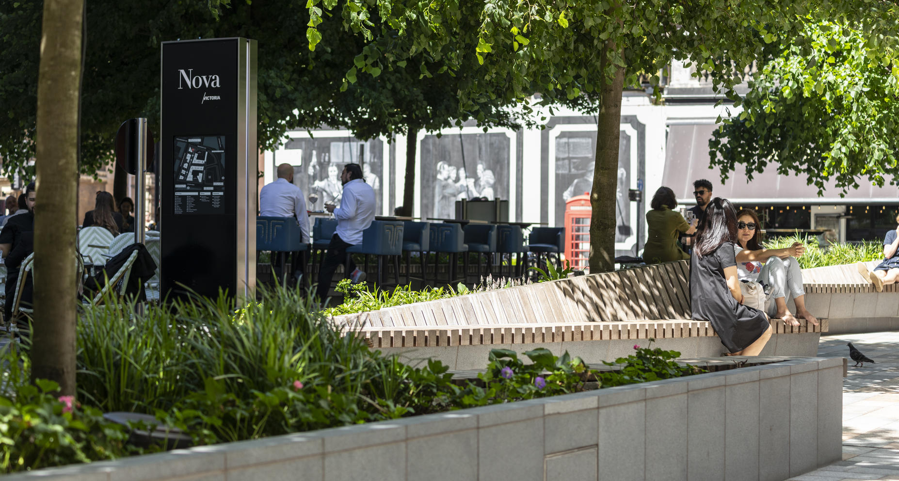 Urban park with Nova signpost, map, benches, trees, and a red telephone booth. (1)