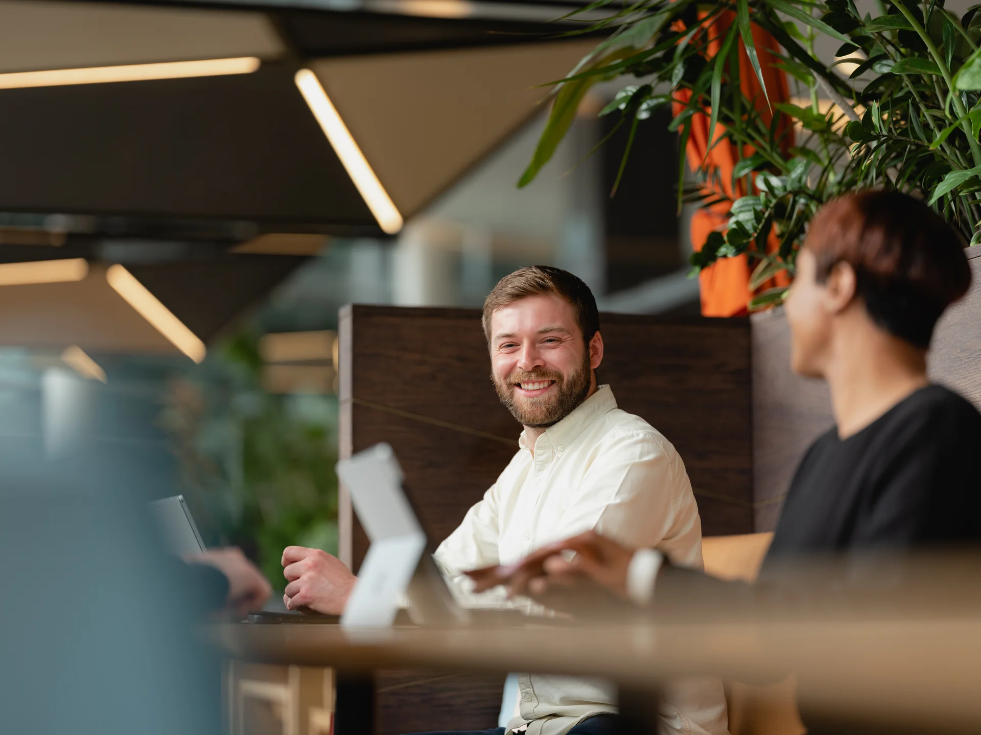 Two individuals collaborate at a modern office desk, surrounded by greenery and contemporary lighting fixtures.