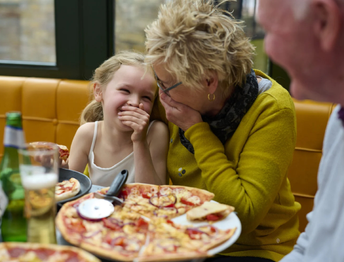 child and two adults eating pizza