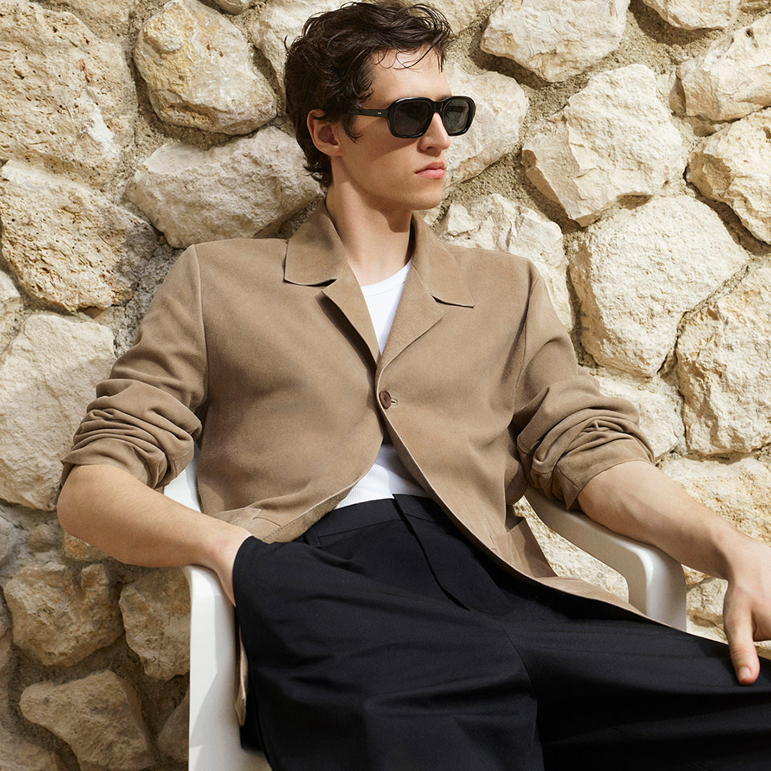 A COS model in front of a brown stone wall wearing a brown shirt and trousers