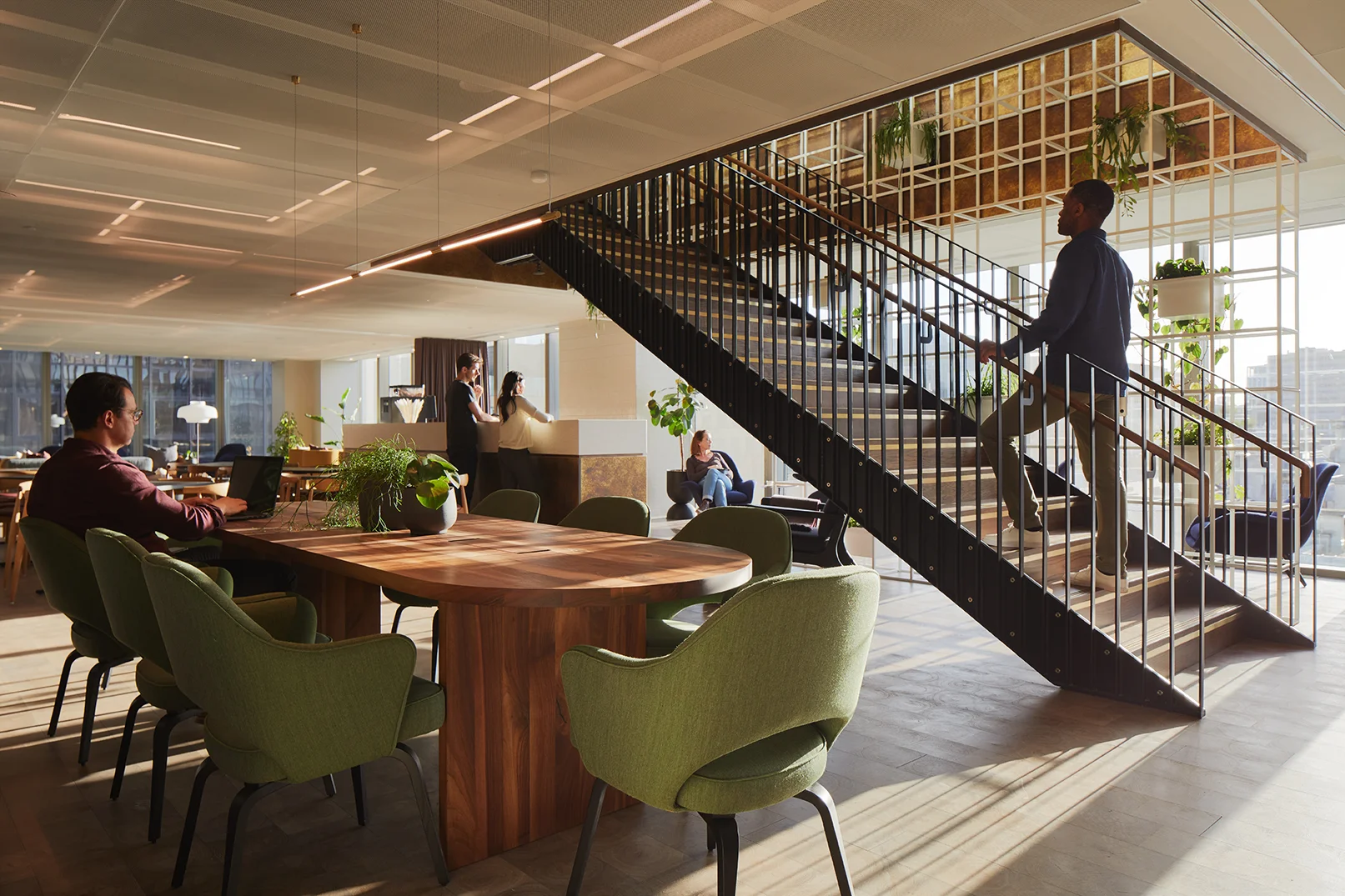 Open office with wood table, green chairs, and a modern staircase