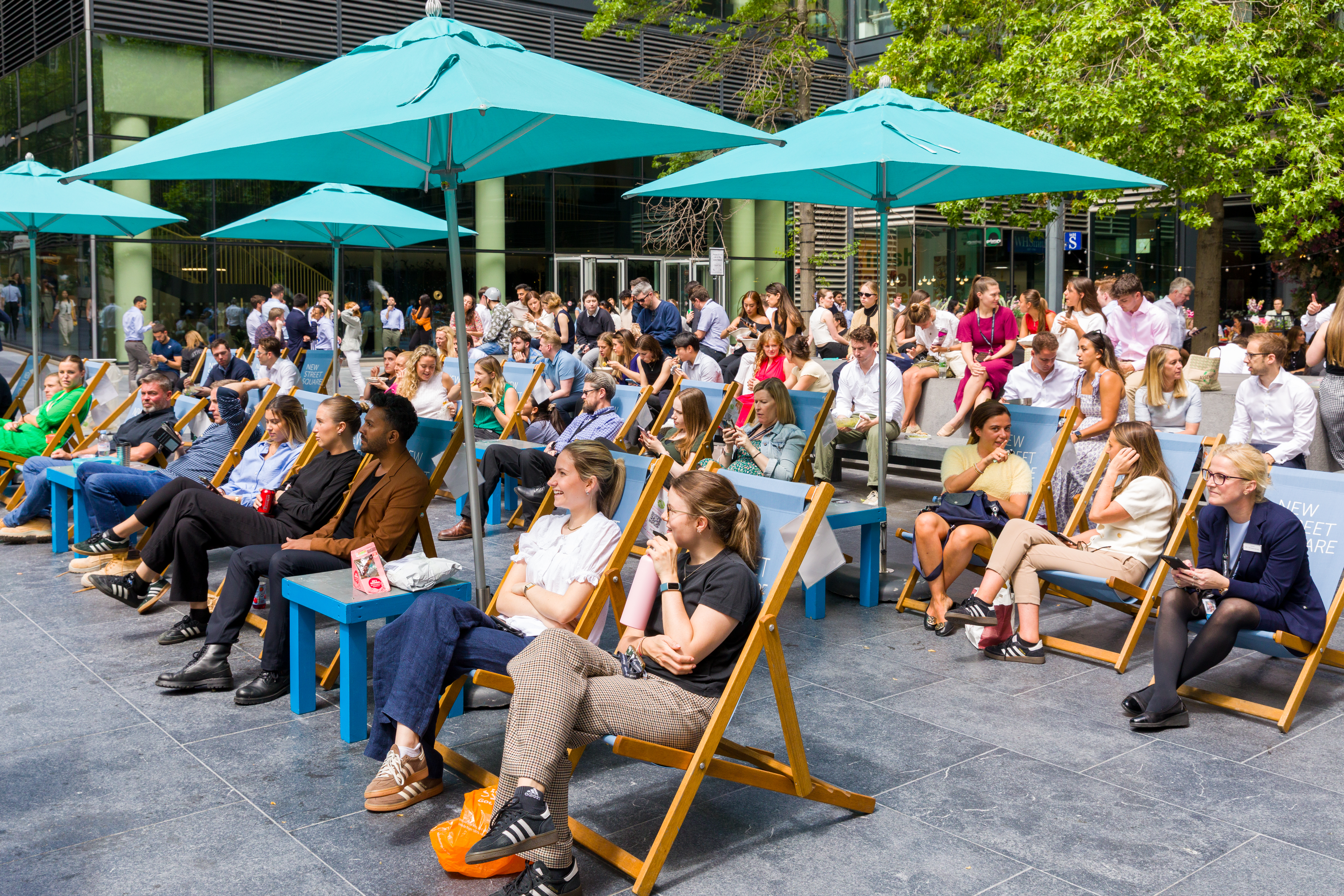 People siting on deckchairs under parasols watching tennis on the big screen