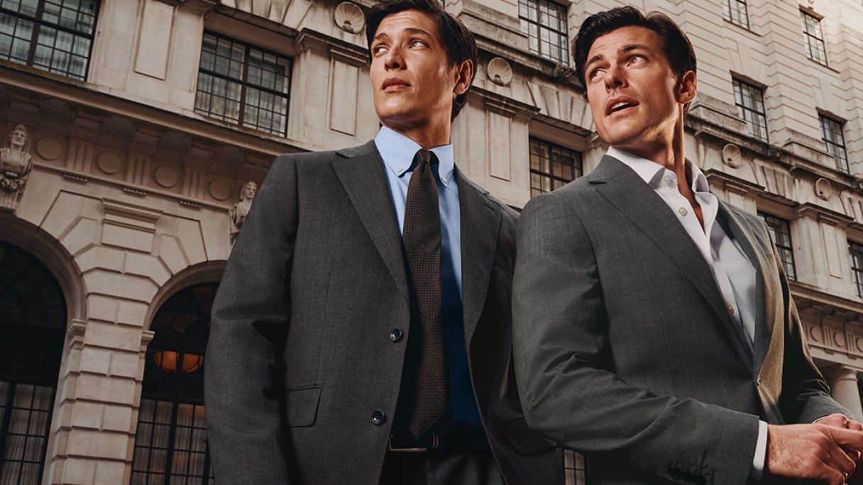 Two men in suits wait outside for a taxi