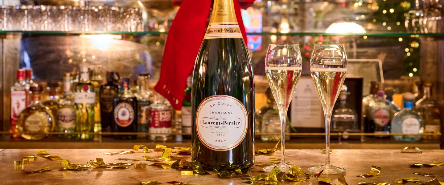 A bottle of champagne on a bar surrounded by glasses and gold confetti