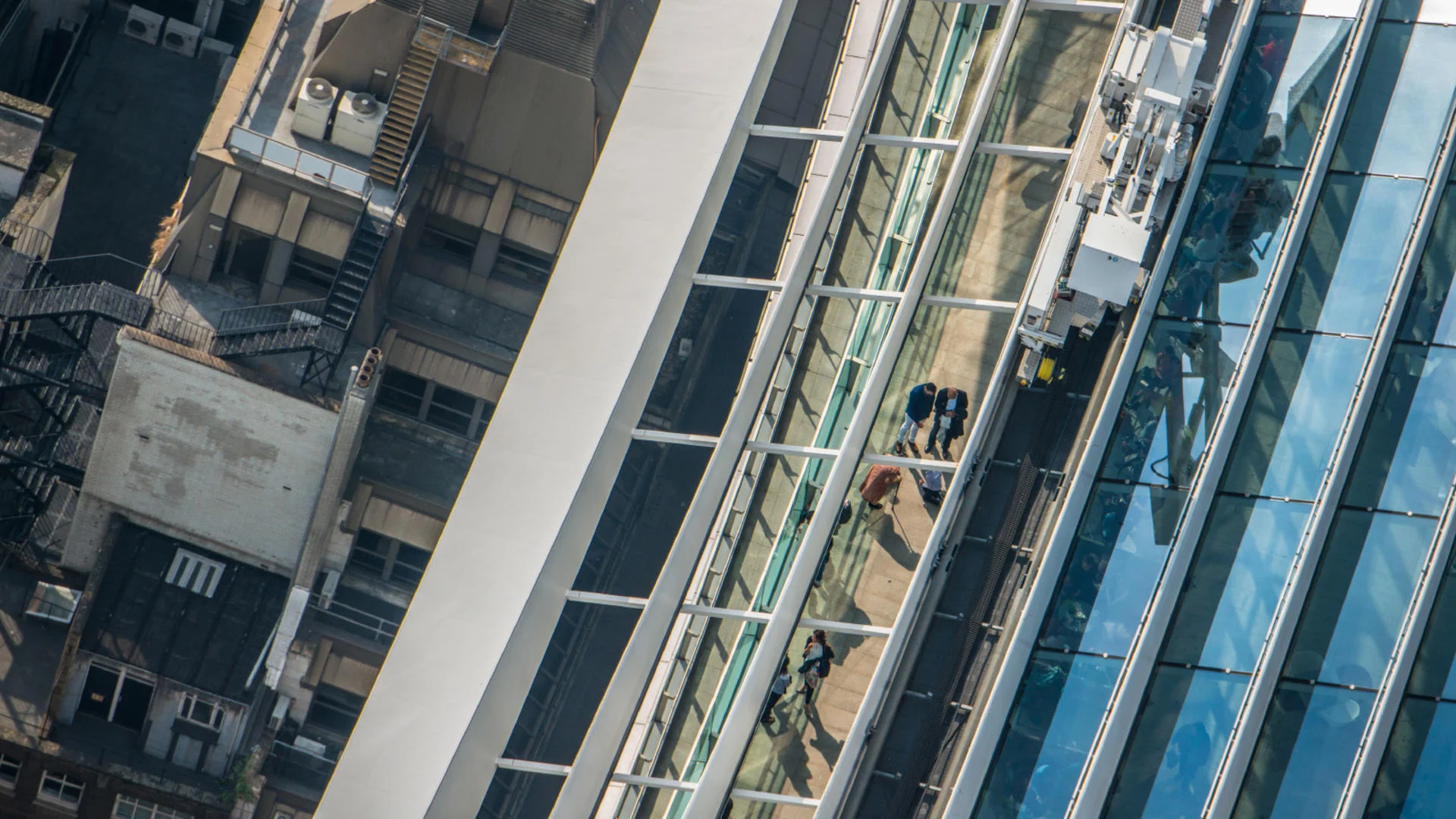 Aerial view of a glass walkway connecting two buildings with people walking on it.