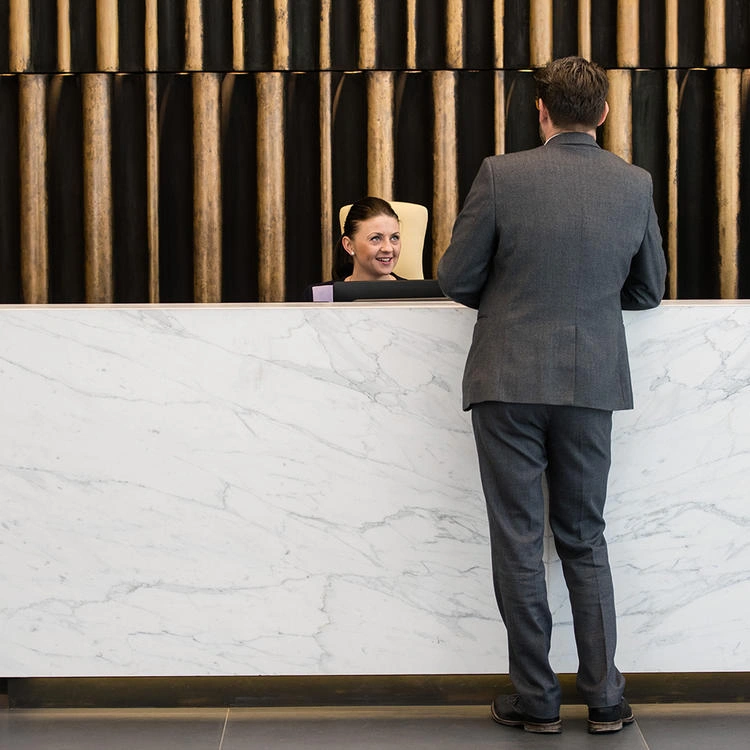 Man in suit speaks to woman at marble reception desk.