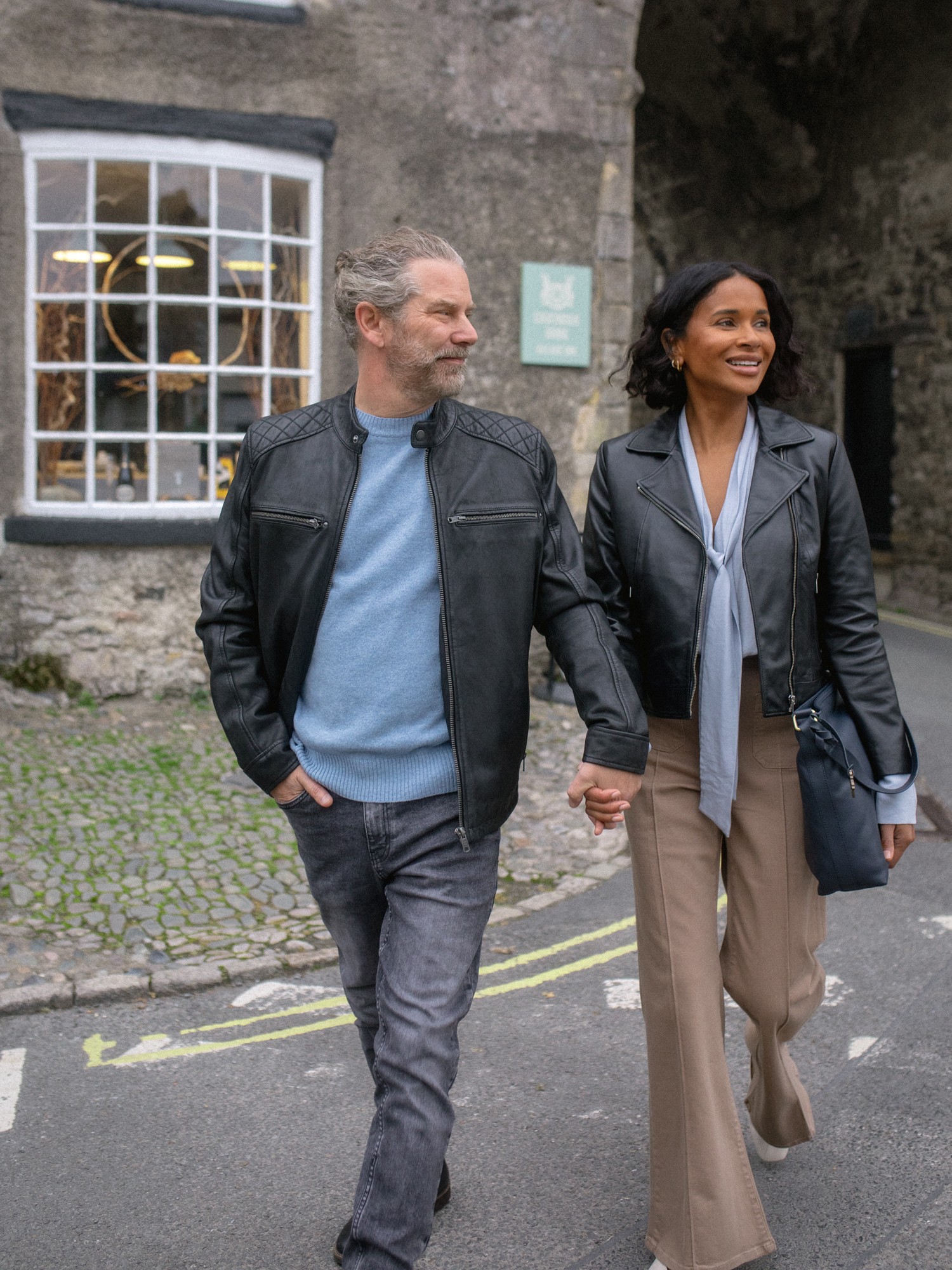 A man and woman wearing leather jacket walk hand in hand