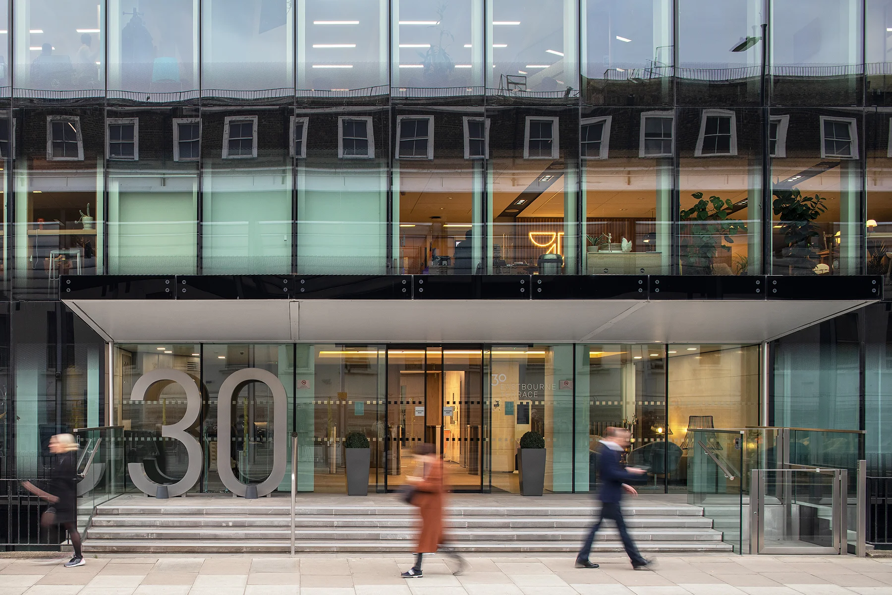 Glass building entrance with large '30' number and people walking