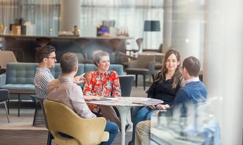 Five people in a modern room having a casual meeting around a table.