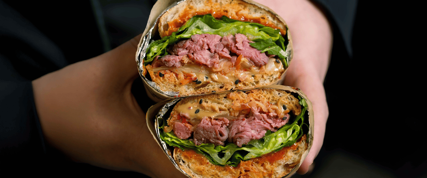 Two hands holding the new Yolk Korean Kimchi Beef sandwich