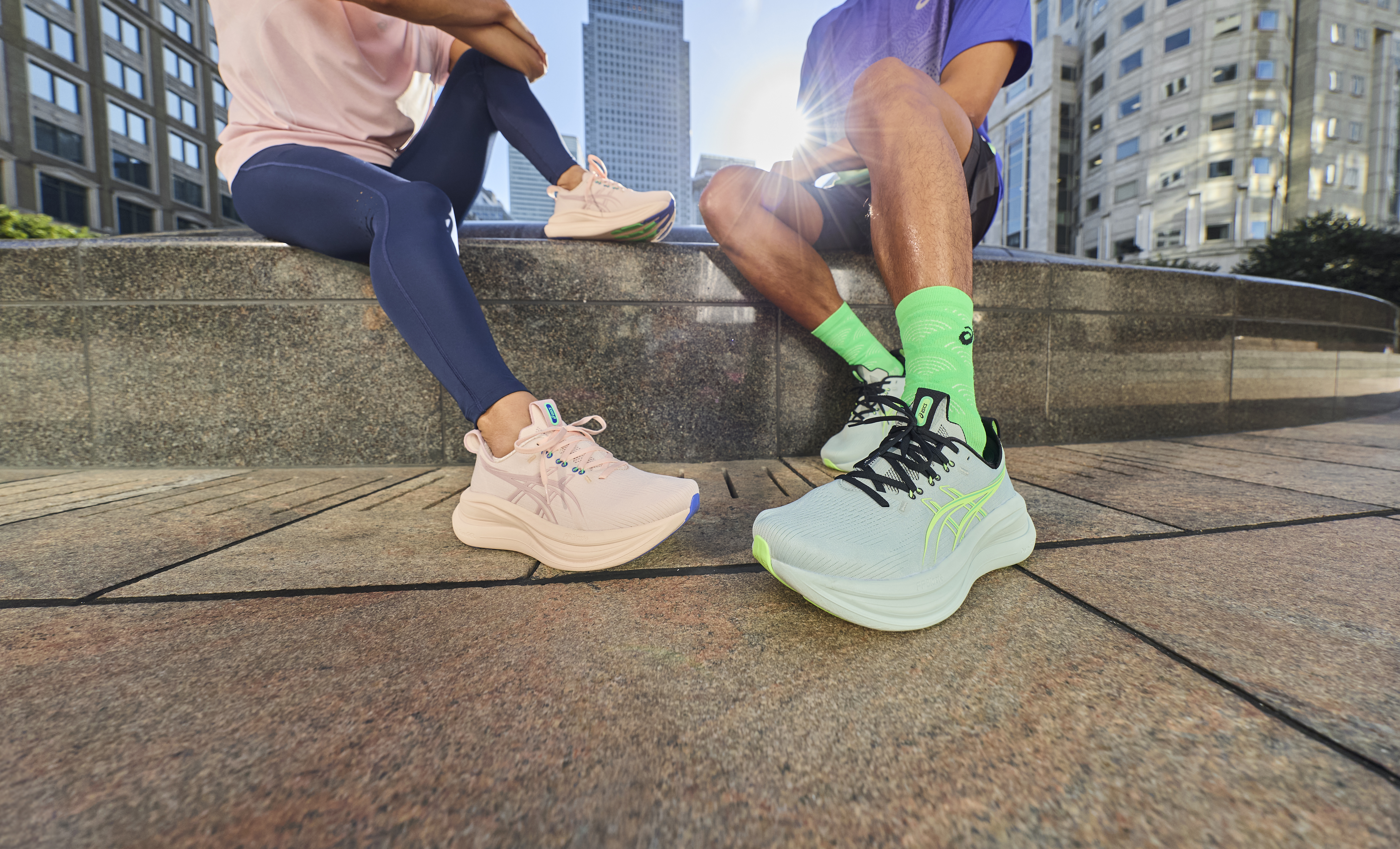 A man and woman wearing sports trainers sit on a city wall