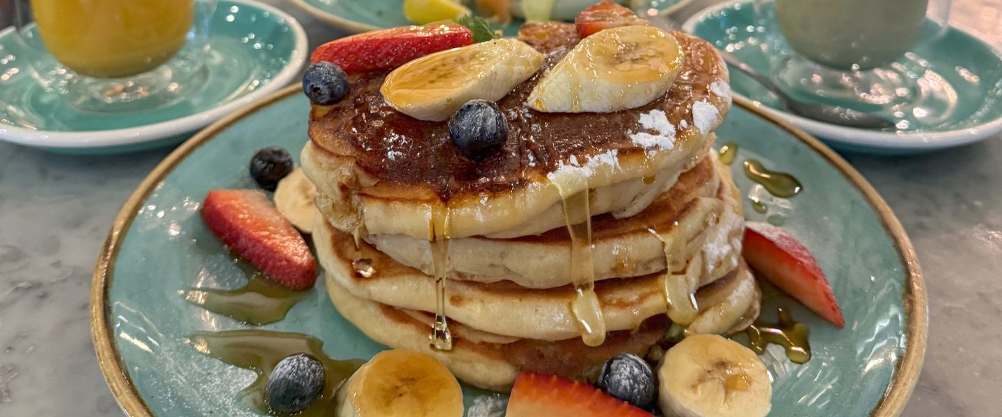 A stack of pancakes topped with syrup, banana slices, strawberries and blueberries