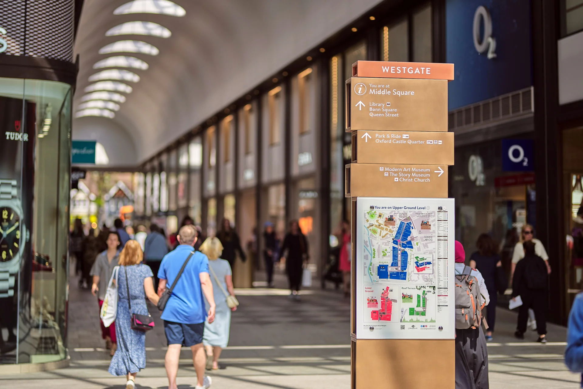 Interior of the **Westgate Oxford** shopping centre, showing a clear directional sign for **Middle Square** and a map of the Upper Ground Level, with shoppers walking in the background.