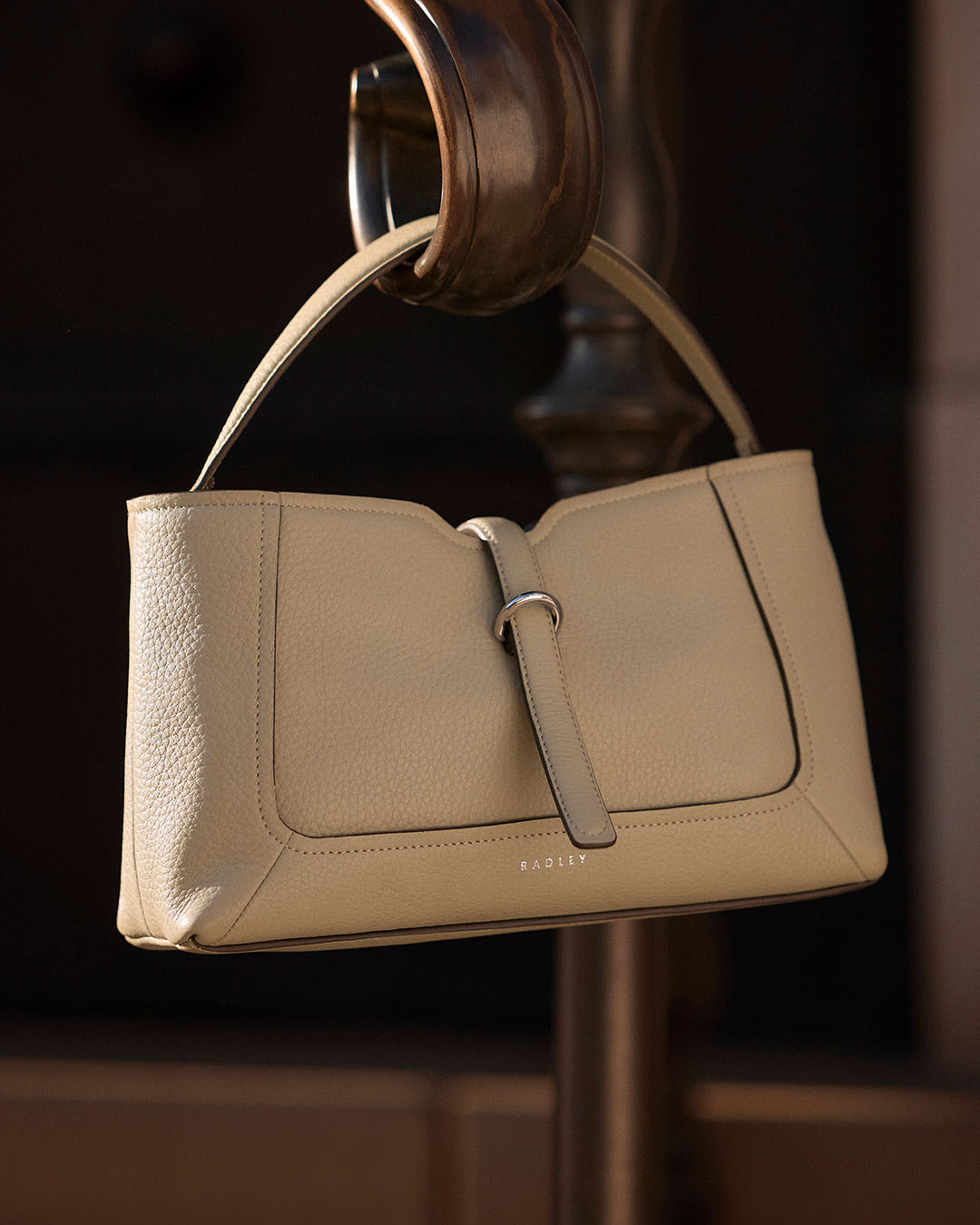 A cream coloured Radley handbag hanging from a curved piece of wood