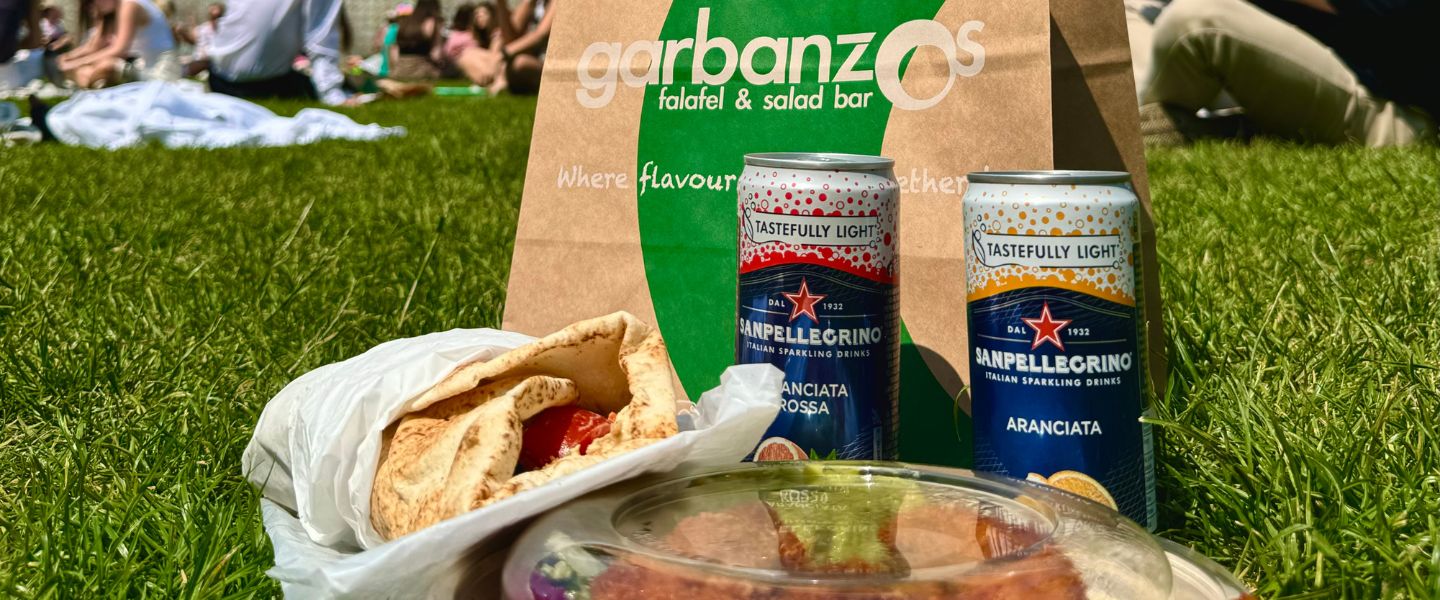 Garbanzos pitta and salad box on the grass with two San Pellegrino cans