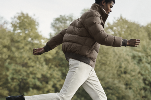 A Reiss model wearing a khaki puffer jacket and white trousers