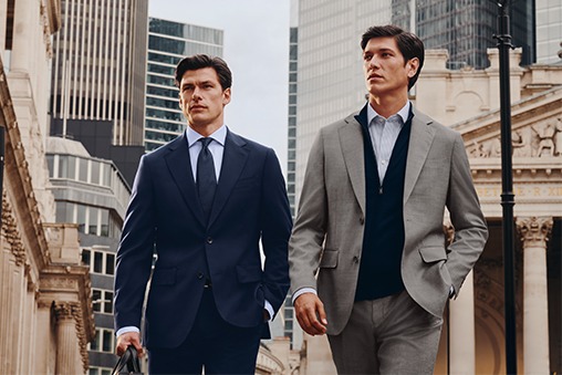 Two men walk down the street wearing suits