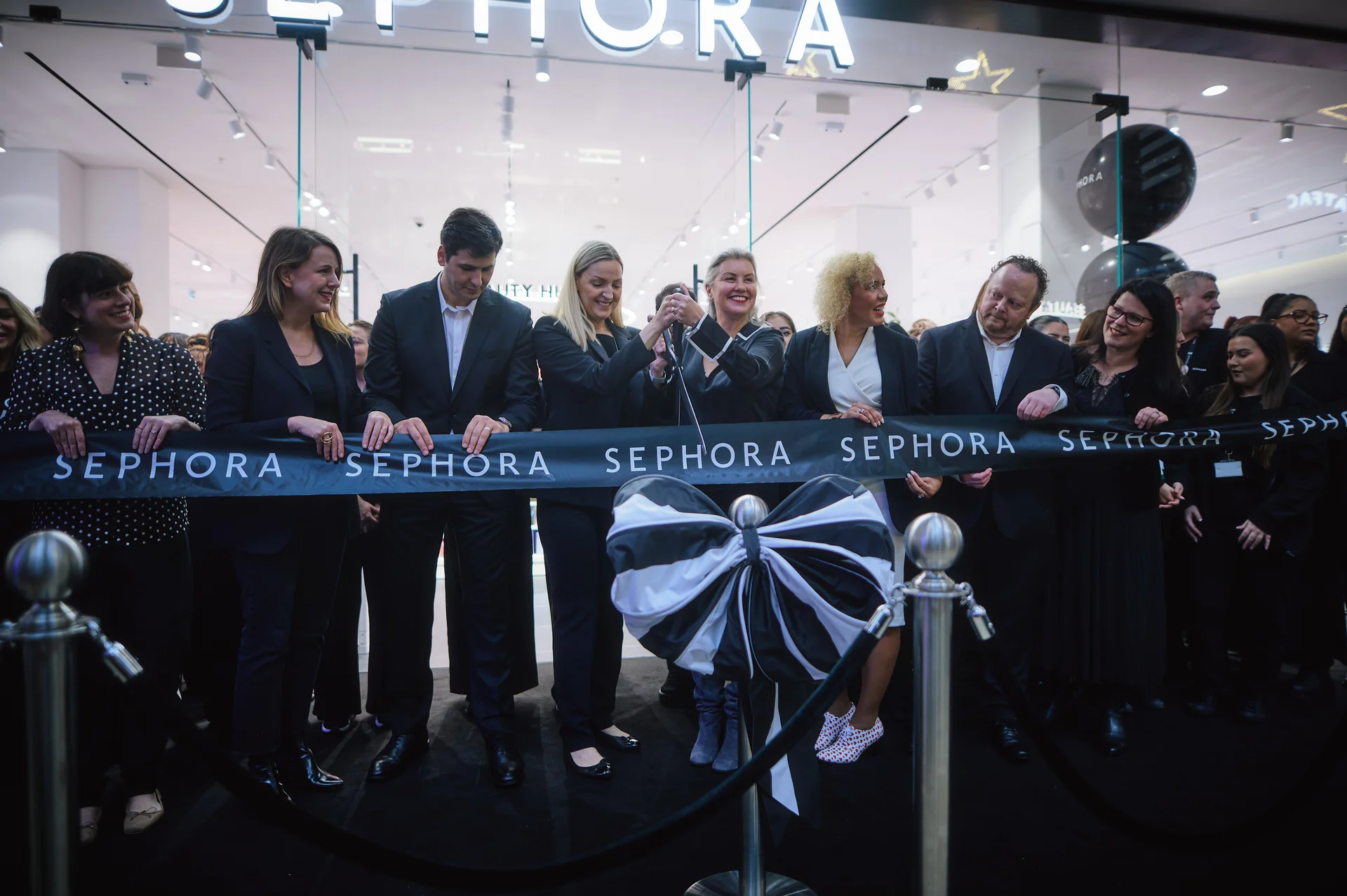 Group cutting a ribbon at a Sephora store opening, with a crowd of onlookers and a modern interior in the background.