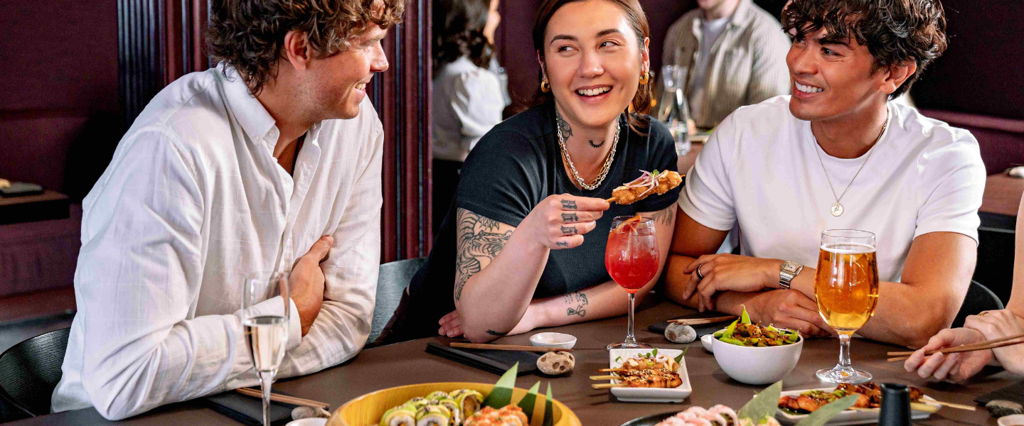 Friends enjoying sushi and drinks at a lively restaurant table, sharing food and conversation.