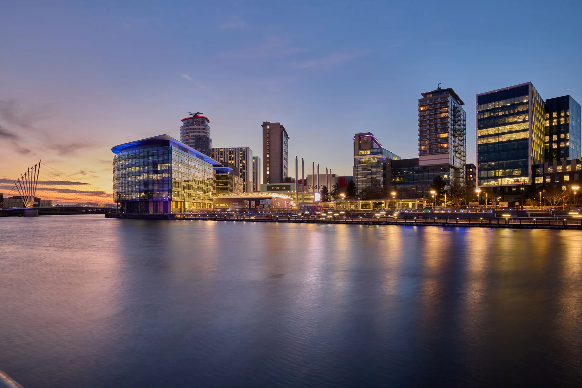 Evening skyline photo of MediaCity UK, Salford, with illuminated buildings reflecting in the water at sunset. Features Dock10.
