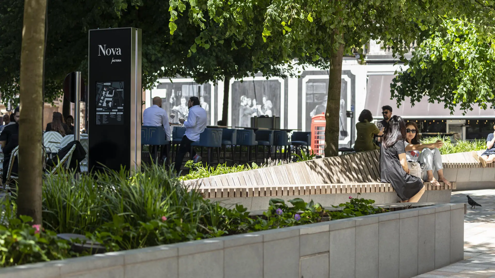 Urban park with Nova signpost, map, benches, trees, and a red telephone booth.