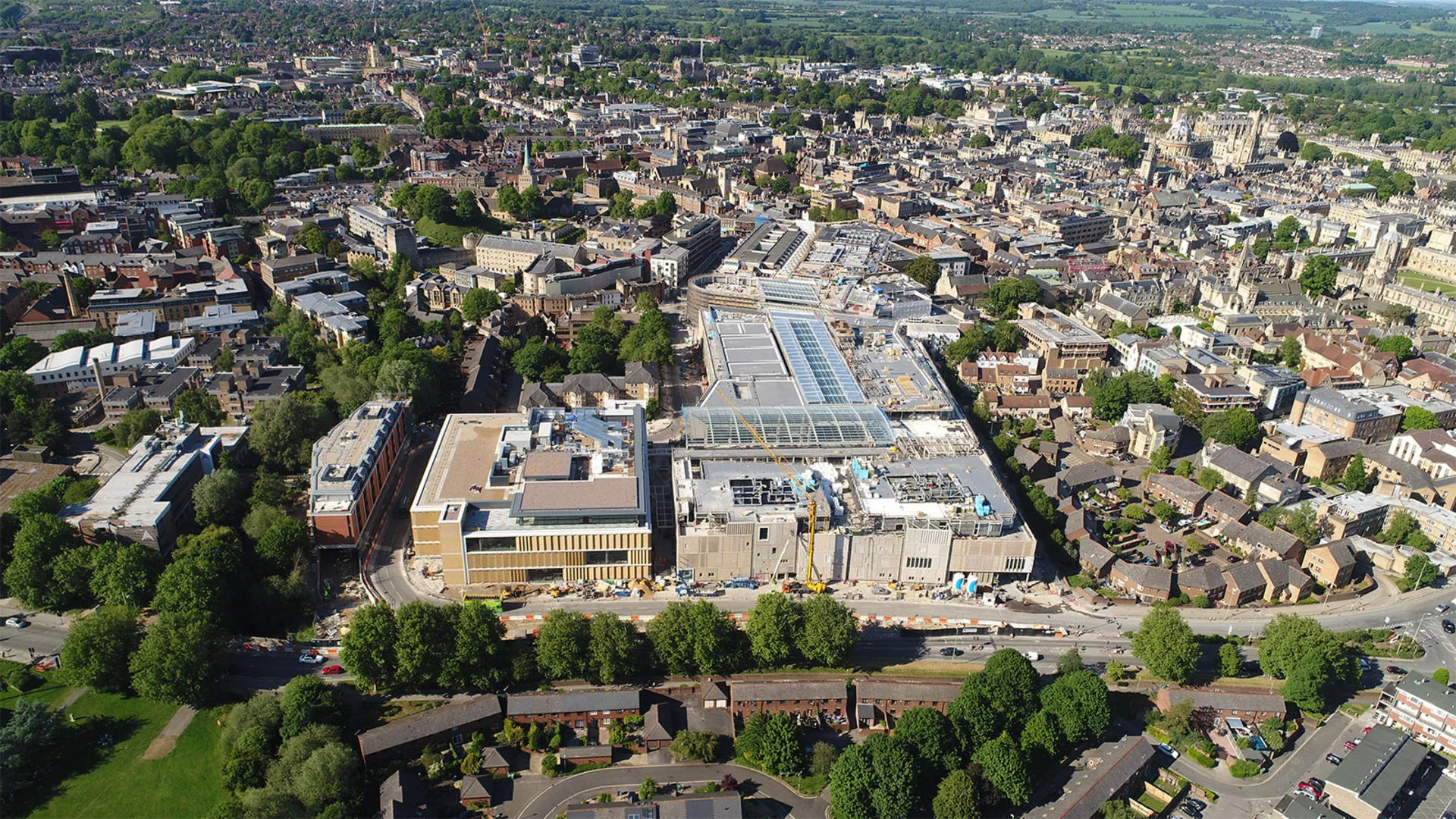 **Aerial view of Westgate Oxford** shopping centre, showing the large modern retail structure integrated into the historic and green landscape of Oxford city centre.