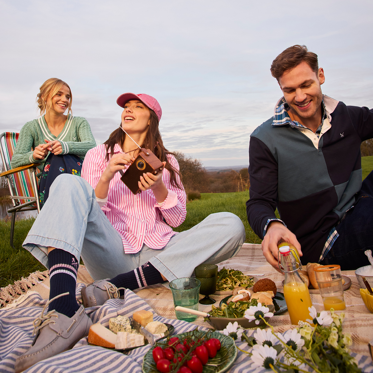 Two young women and a man, possibly family, or friends having a picnic and laughing  