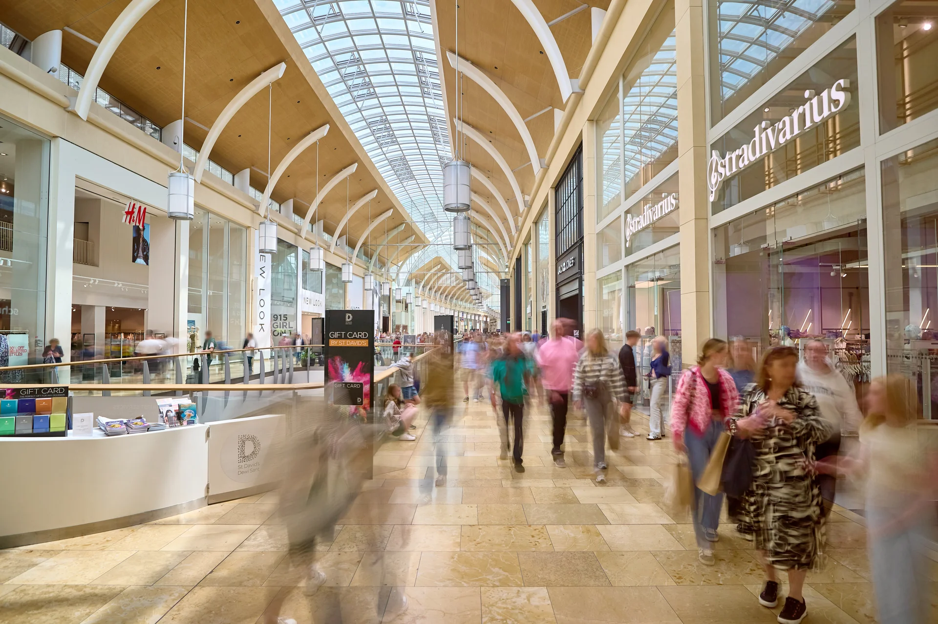 Bright St David's Cardiff shopping centre, showing Stradivarius, H&M, and a wide, busy walkway.