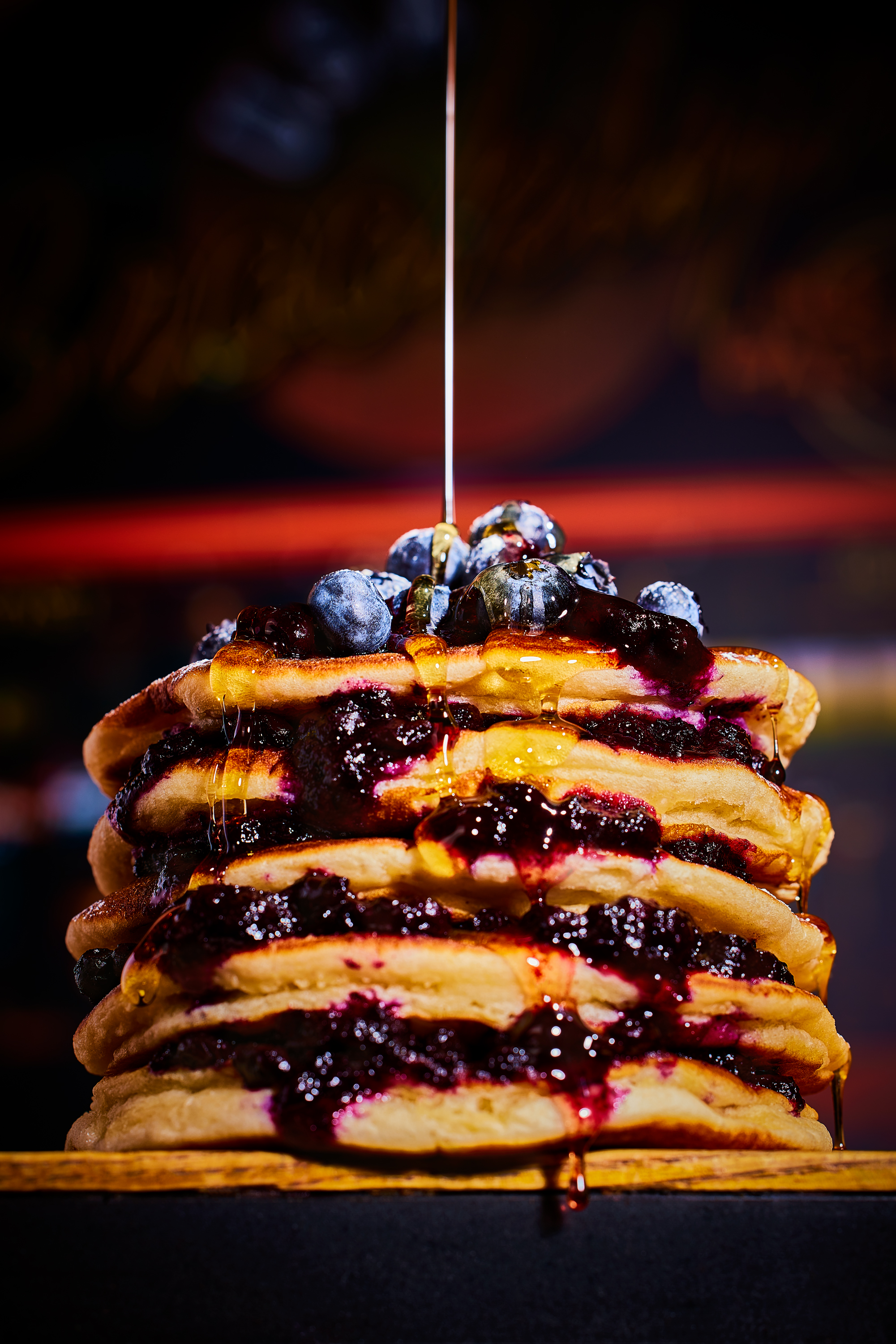 A stack of five bluberry pancakes and drizzled syrup and fresh bluberries 