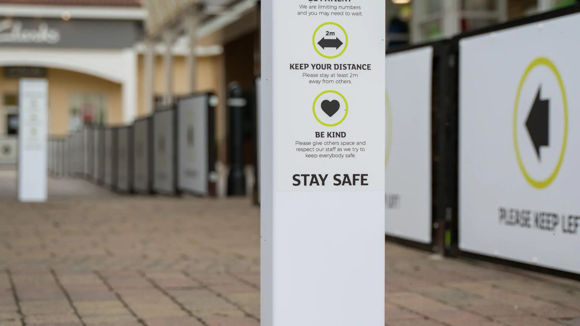 Sign with social distancing guidelines including "Keep Your Distance 2m", "Be Patient", "Be Kind", and "Stay Safe".