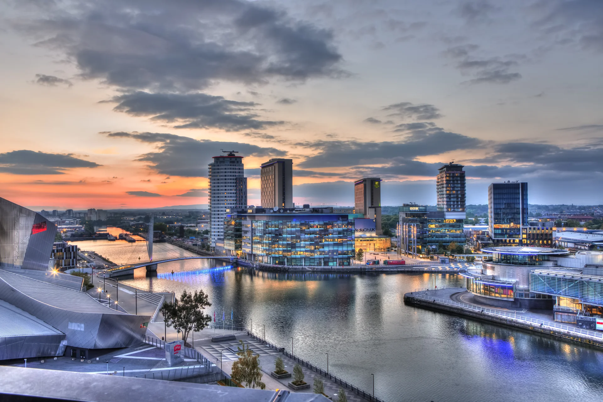 A stunning evening photograph of the MediaCityUK development in Greater Manchester, highlighting the architecture of the towers and studios reflecting on the quayside water.