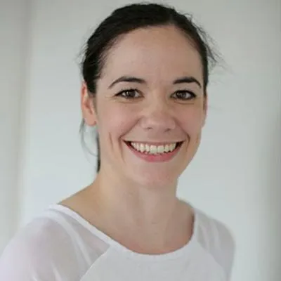 Woman with dark hair in a white top smiling.