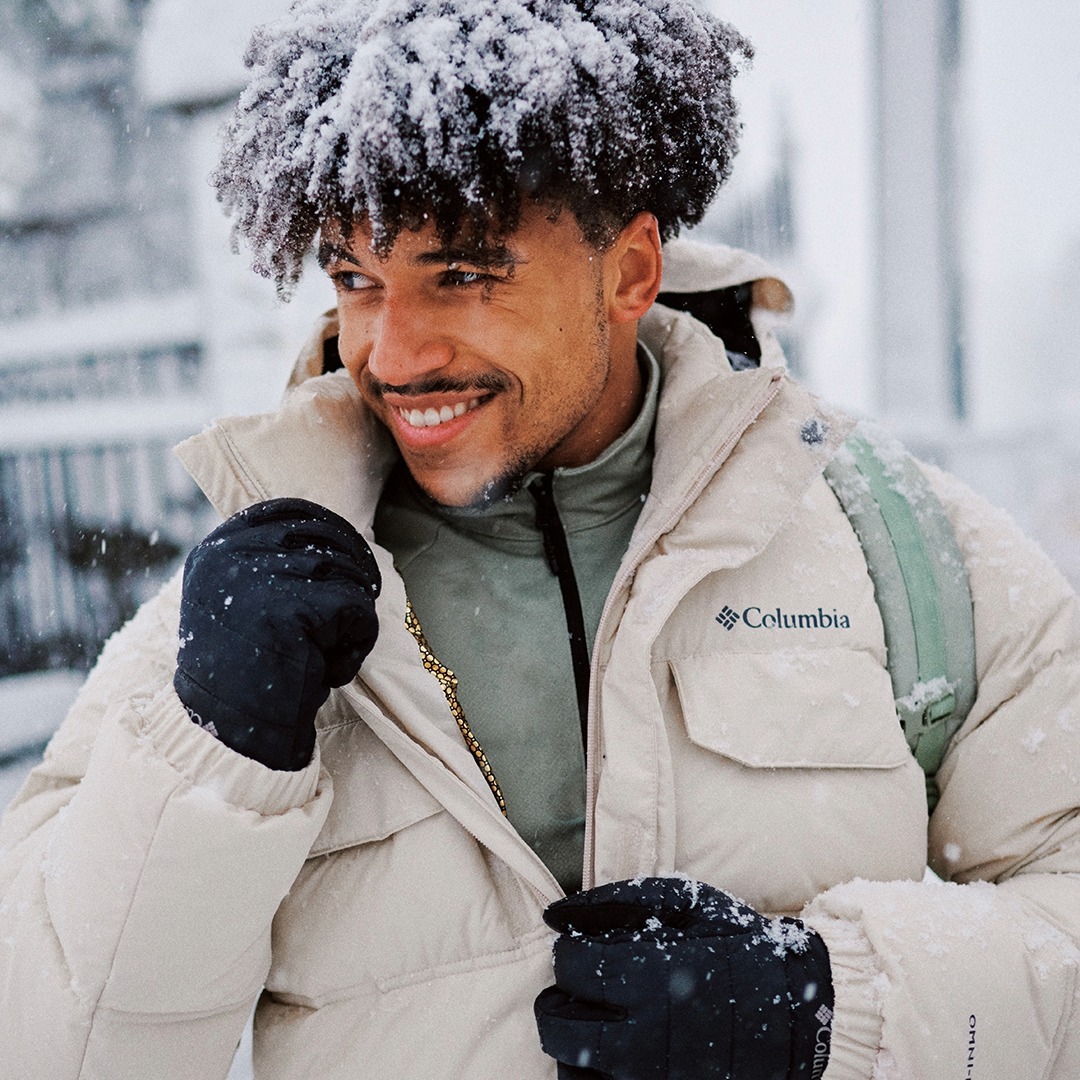 A man with snow-topped hair holds his winter coat collar in his gloved hands