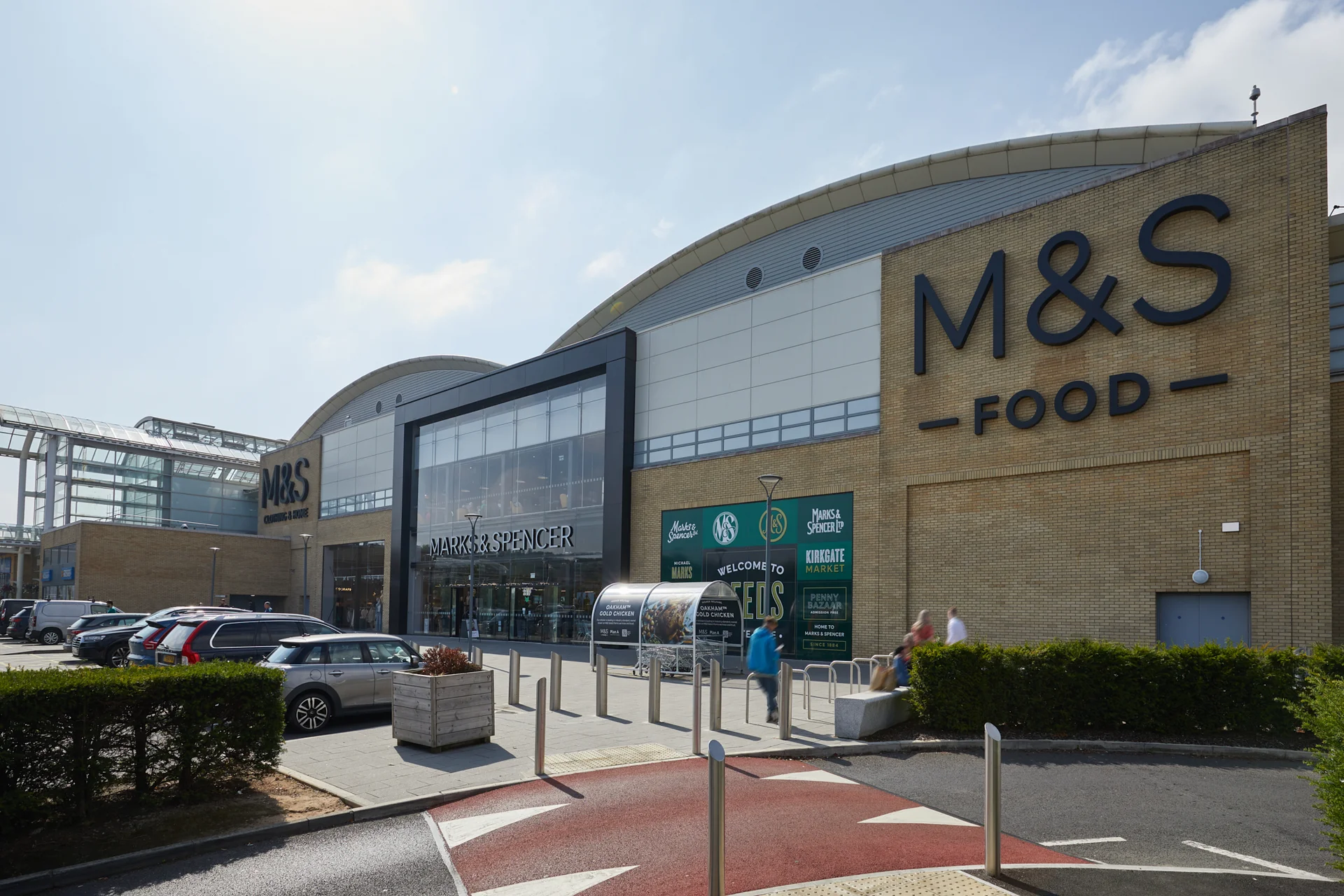 Exterior view of the White Rose Shopping Centre in Leeds with the M&S Food entrance and people walking outside.