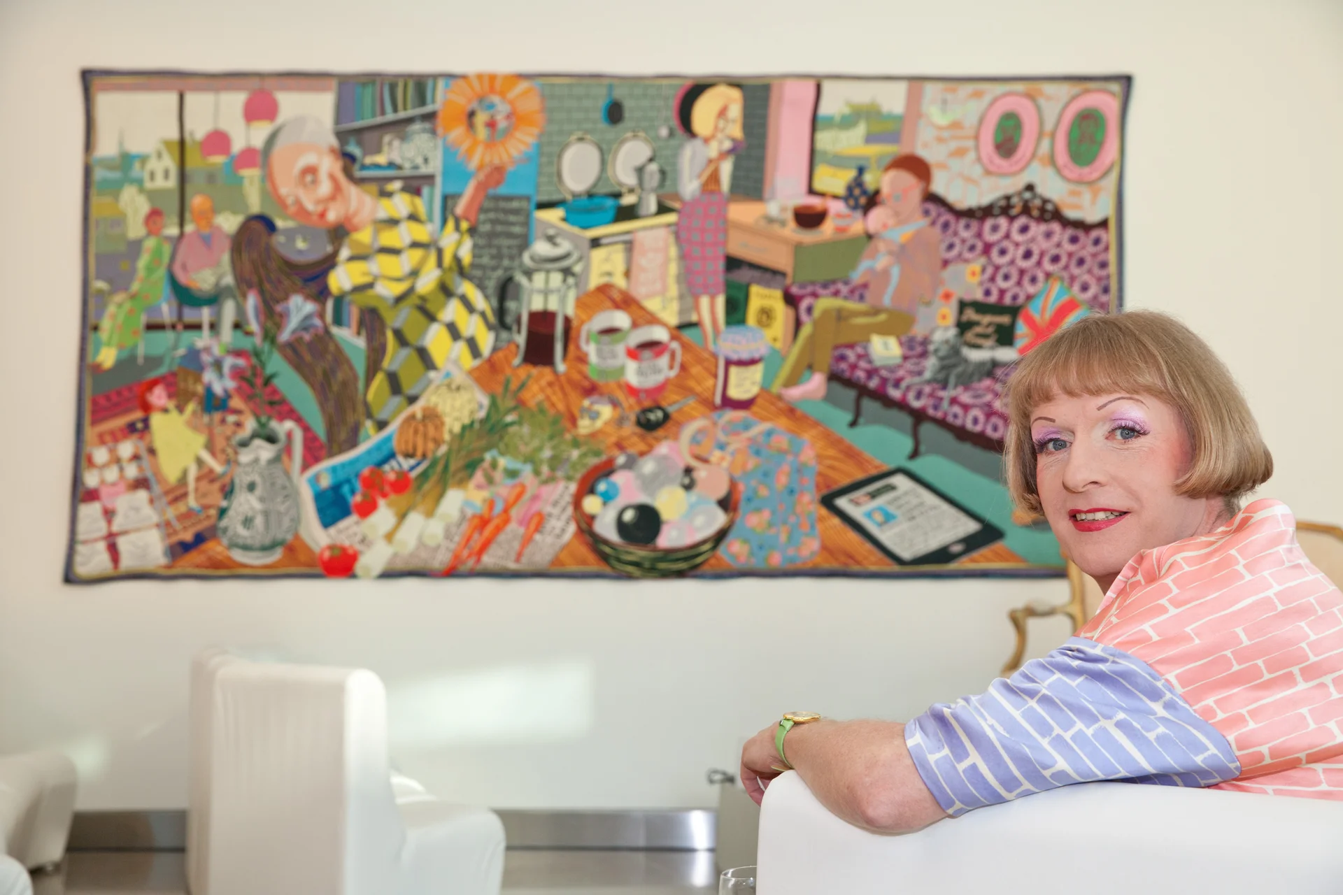 Artist seated in front of a colorful tapestry artwork