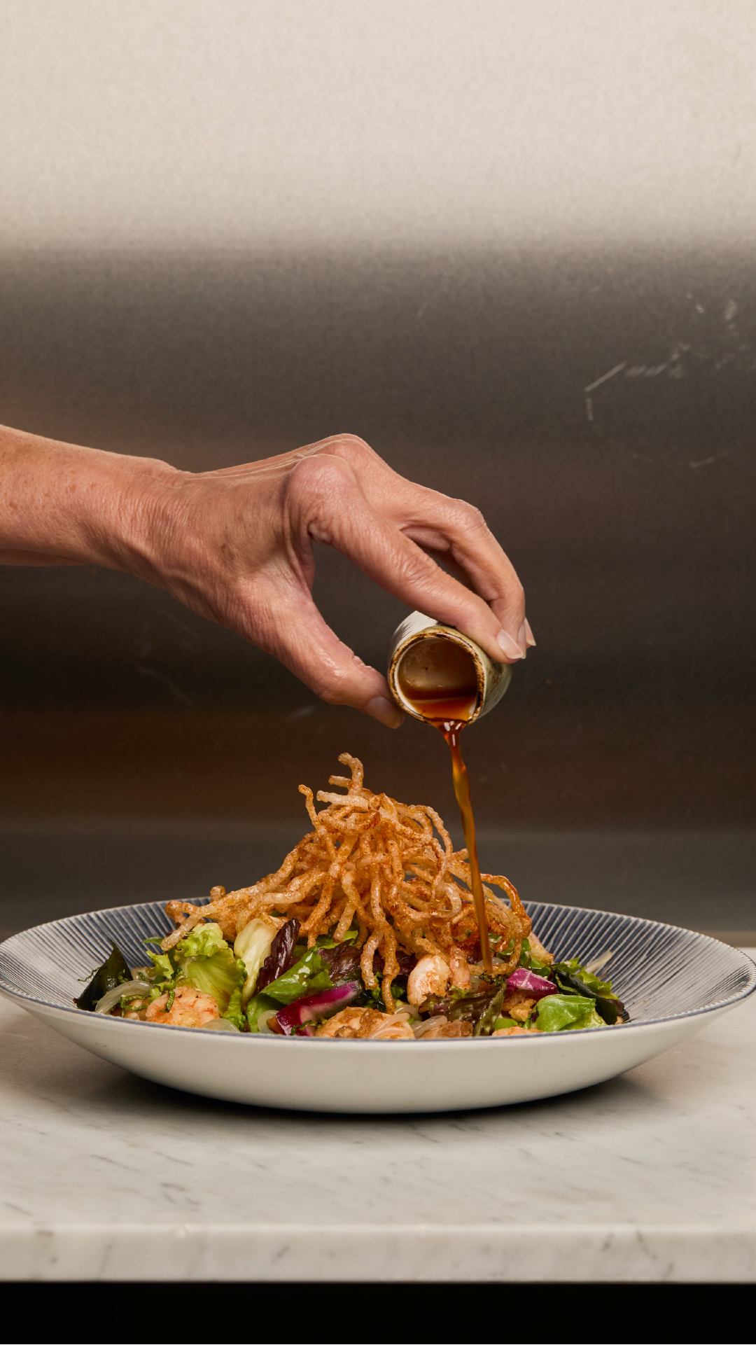 wagamama salad with a person's hand pouring sauce on top