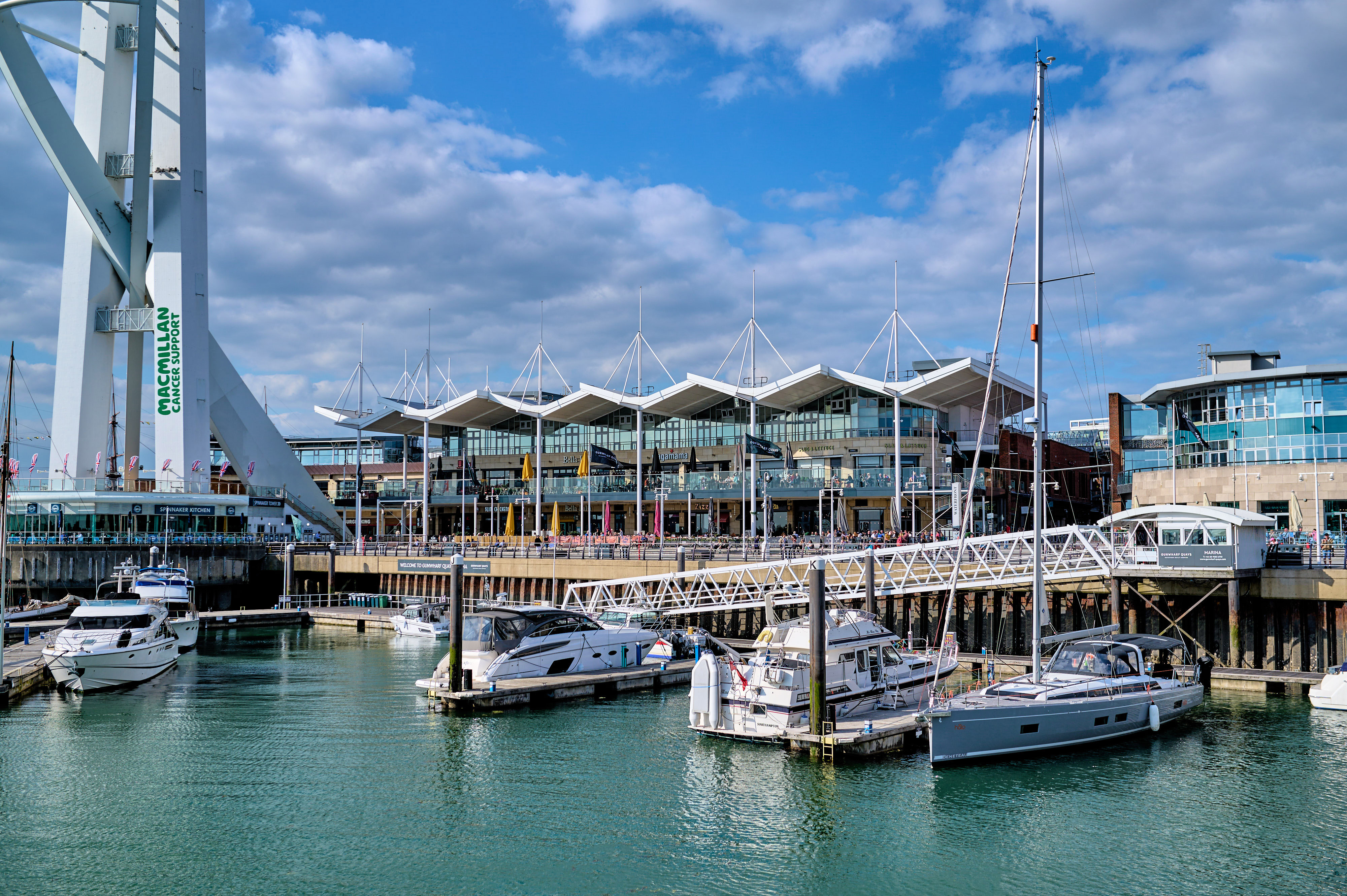 Drone shot of Gunwharf Quays that includes the waterfront, marina, and the Spinnaker Tower against a blue sky.