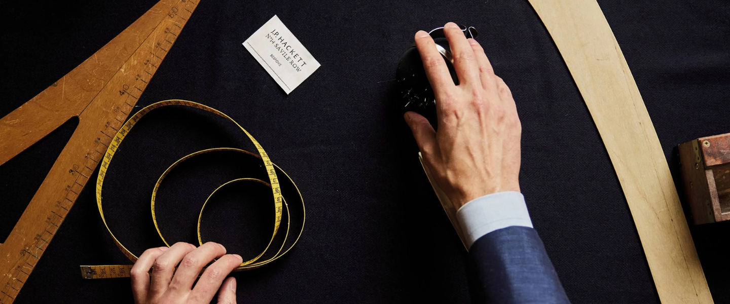 Tailor’s workspace with measuring tape and tools on fabric, showcasing bespoke menswear craftsmanship.