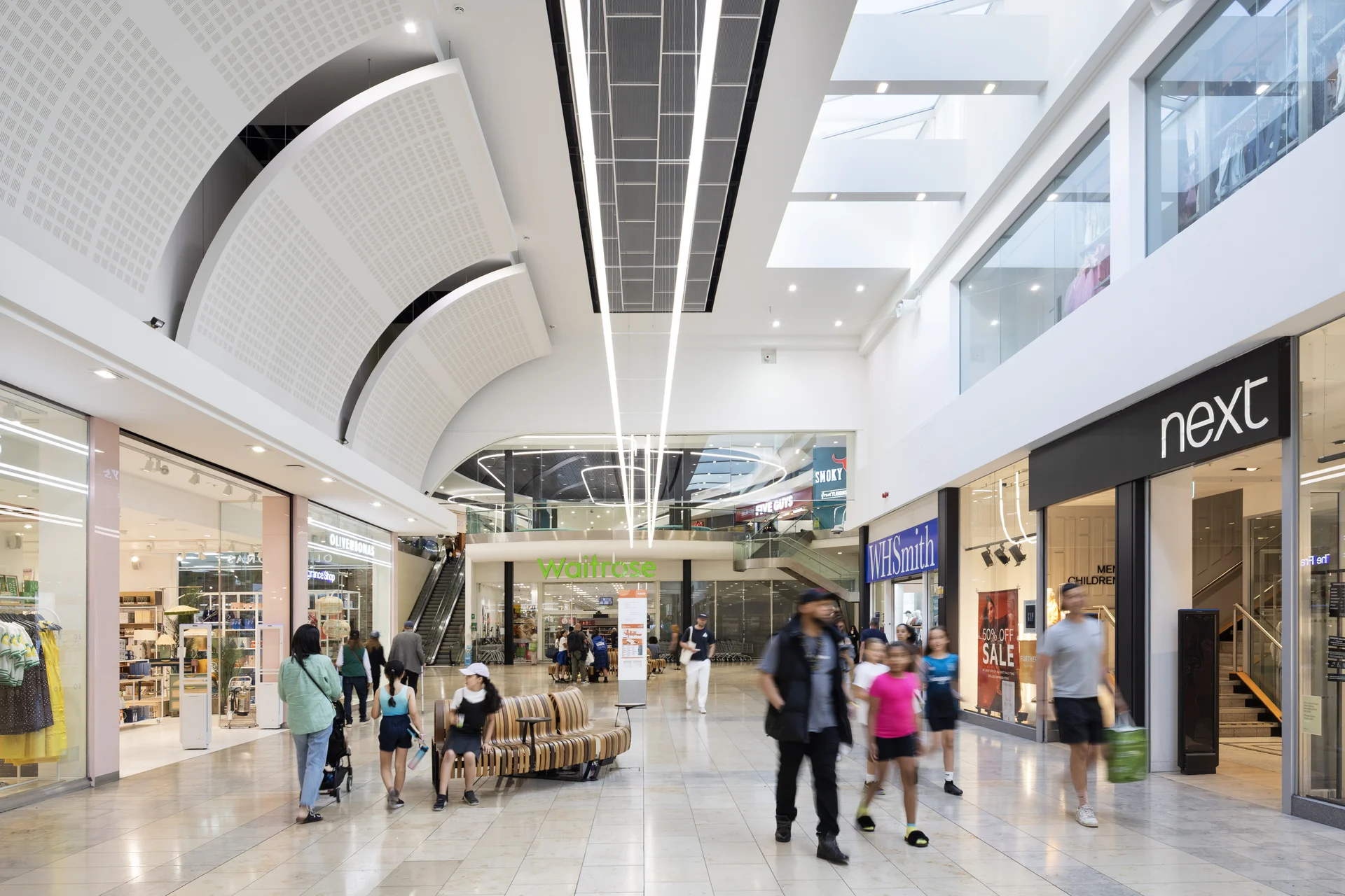 Bright interior of **Southside Shopping Centre** in Wandsworth, showing the main atrium with a **Waitrose** supermarket entrance, escalators, and **Next** retail store, with shoppers walking through.