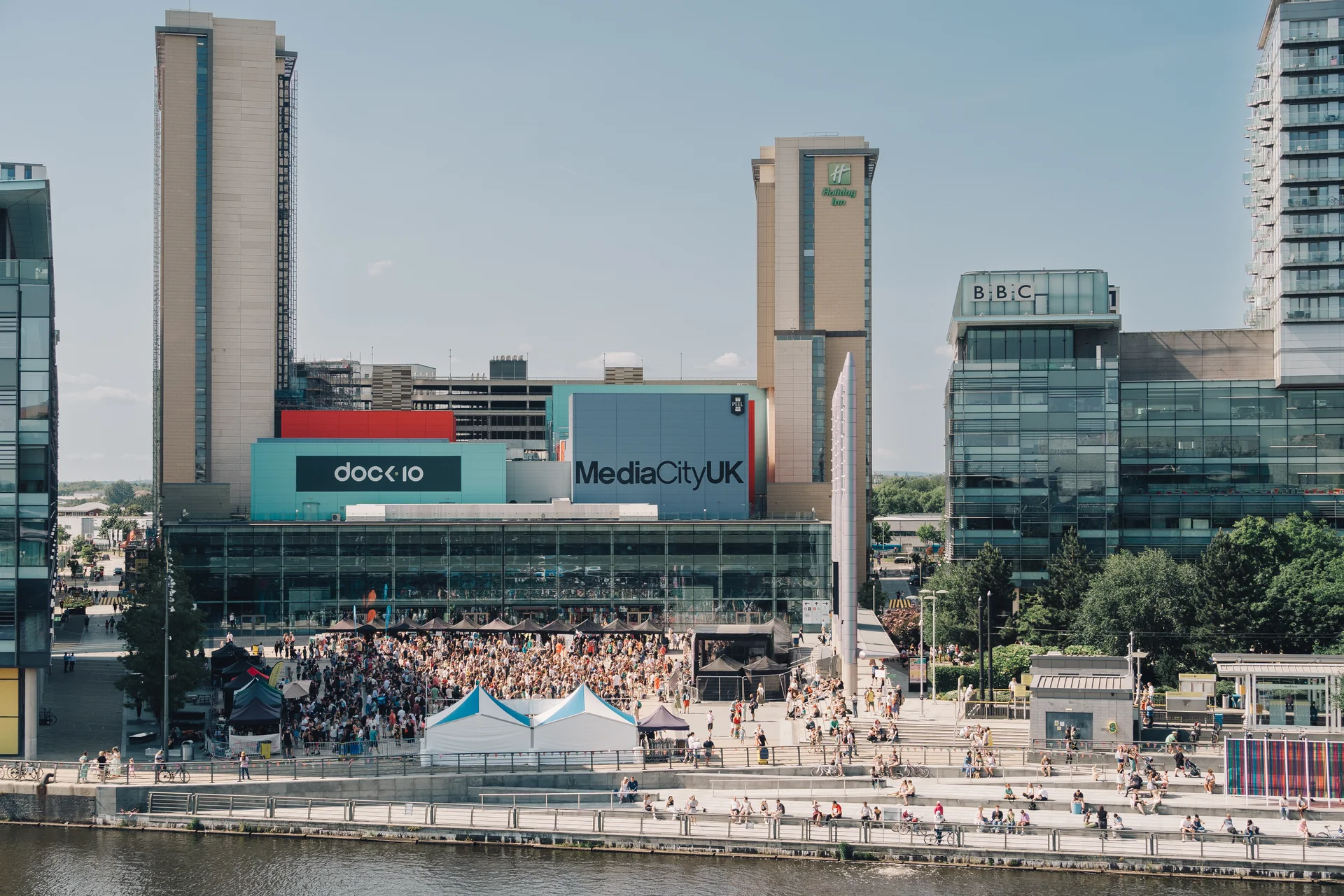 Wide view of the MediaCityUK Piazza with a large crowd attending an event, featuring the BBC and Dock10 buildings.