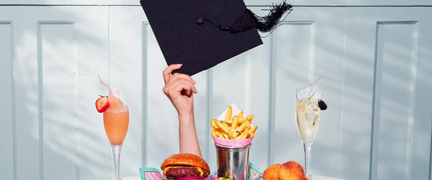 Someone holding a graduation cap behind a table of food and drinks